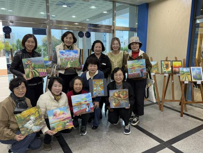 힐링아트(오일파스텔) 전시회’ 현장에서 사천시복지청소년재단 경영본부장(변은진), 강사(박홍은), 회원들이 전시 성료를 기념하며 단체사진을 촬영하고 있다.