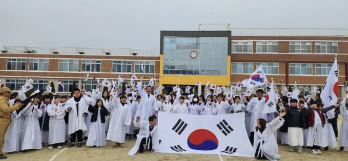 제5회 온양지역 3·11만세운동 재현행사에서 참가자들과 온양초 학생들이 대형 태극기와 함께 힘차게 만세를 외치며 기념촬영하고 있다.